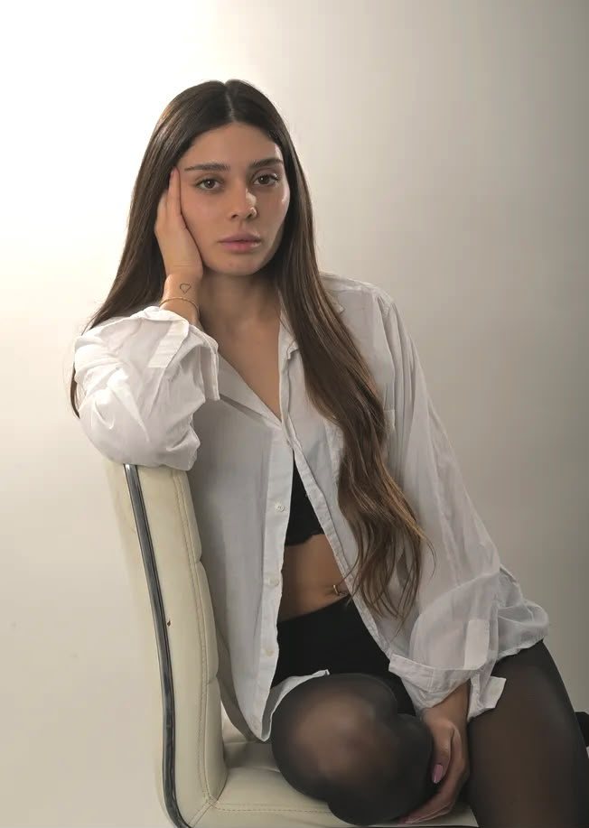 פורטרט סטודיו של אישה בחולצה לבנה יושבת על כיסא, רקע בהיר