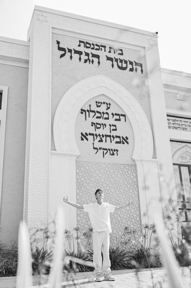 תמונת שחור־לבן של נער בזרועות פרושות מול בית כנסת